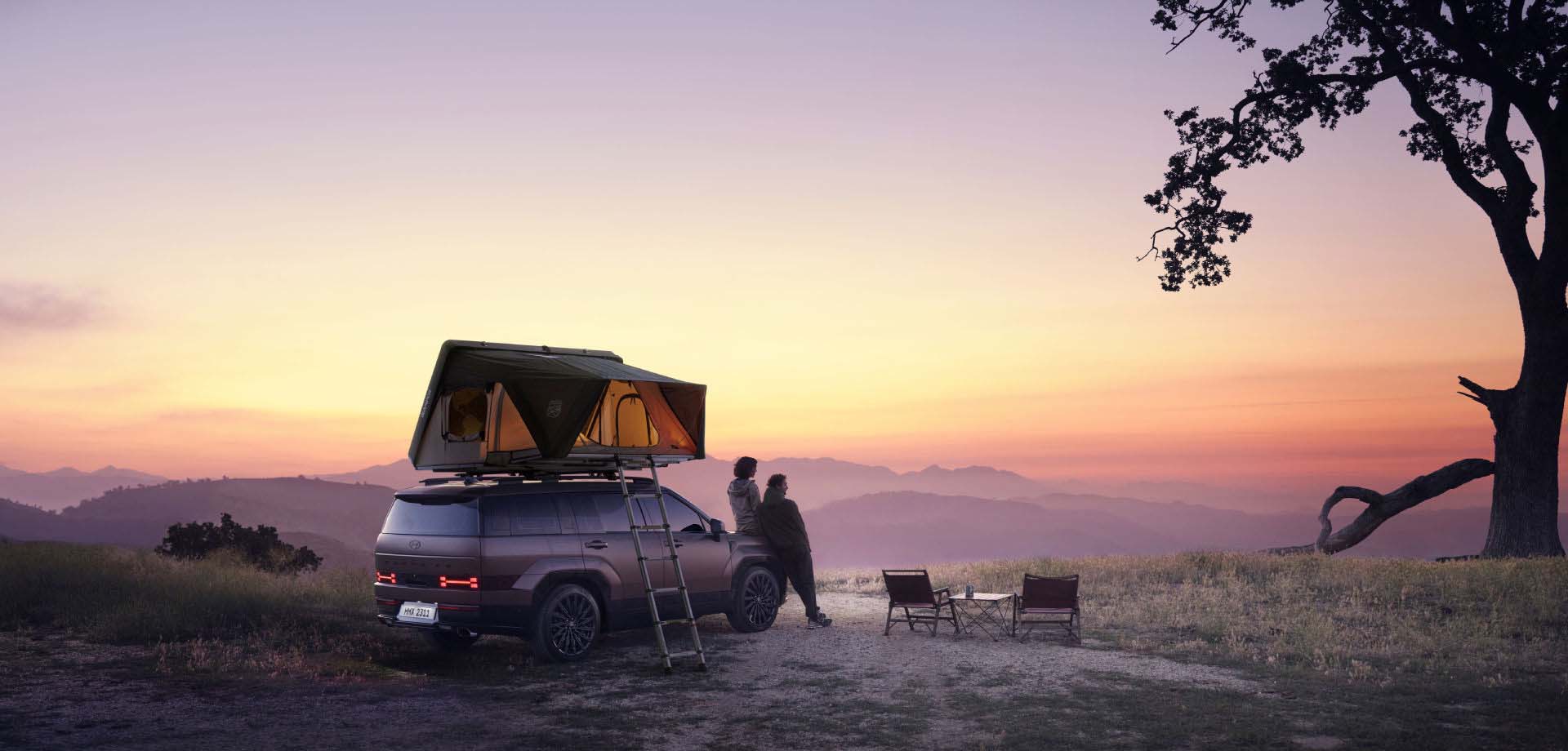 Two men and a women are positioned in front of a SANTA FE, a tent pitched nearby, all of them gazing at the captivating sunset.